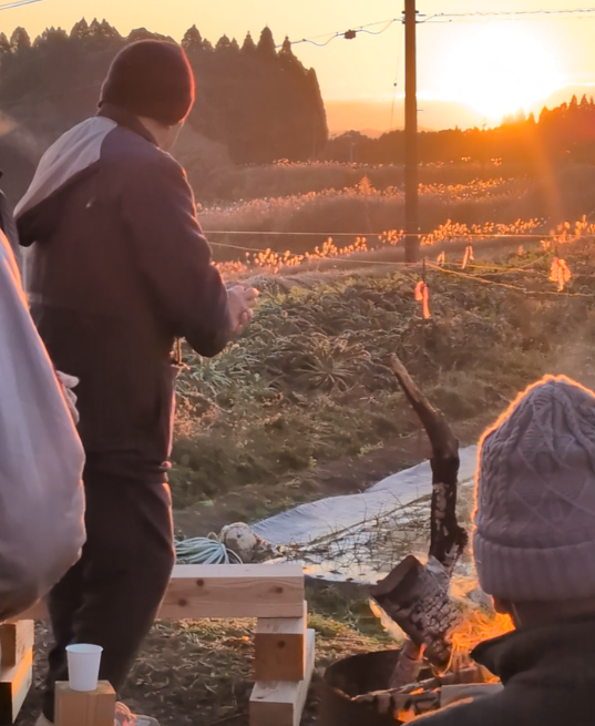 地域の方々と焚き火で暖を取り焼酎を飲んだりぜんざいを食べながら初日の出を見る様子